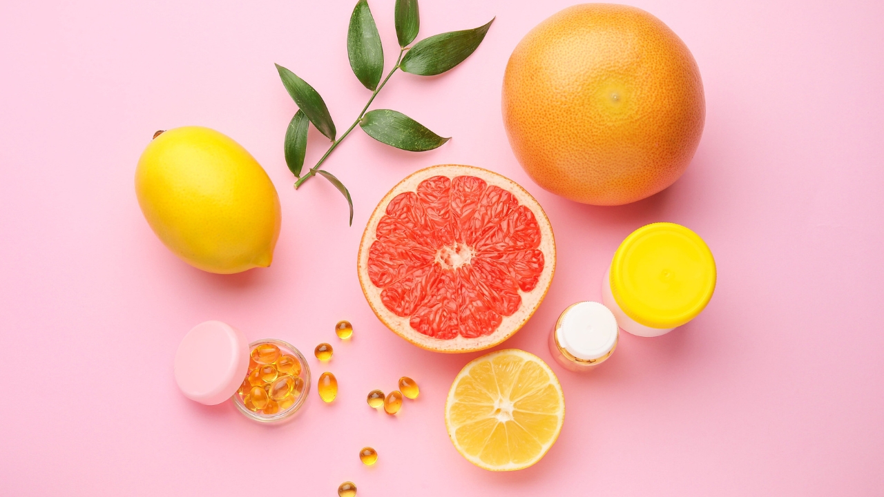 Citrusi i suplementi vitamina na roze pozadini.