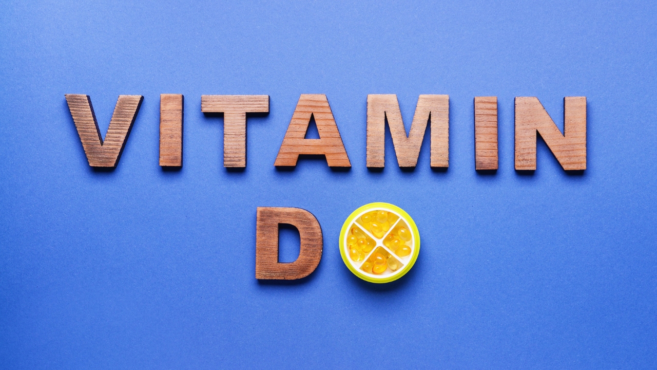 Drvena slova Vitamin D i kapsule na plavoj podlozi.